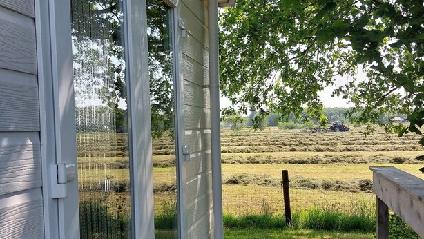 A view from a window overlooking a rural landscape with hay bales and a tractor in the distance. - Cosy Holiday Home in Appelscha With a Great View (Appelscha)