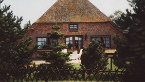 Una casa de ladrillo con techo triangular, una valla de madera y árboles en primer plano.