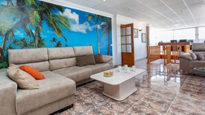 A spacious living area with a large sofa, a coffee table, and a mural of palm trees on the wall. - Apartment Jazmin by Interhome (Salou)