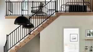 A spacious loft with a high ceiling, a central island with a kitchen, a staircase, and a living area with a sofa and a rug. - Waterview. Hot Tub. Gas Firepit. Lancaster 40 min. (Airville)