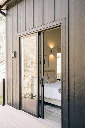 Une chambre avec une porte-fenêtre coulissante, un lit avec une literie blanche et une table de chevet.