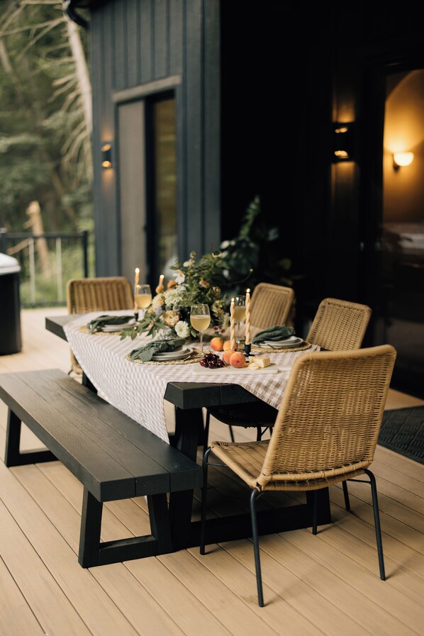 Un espace de restauration en plein air avec une table dressée pour quatre personnes, comprenant des chaises en osier, un banc et une nappe à carreaux.