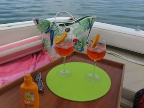 A tray with two drinks, a bottle of sunscreen, and a colorful bag on a boat.