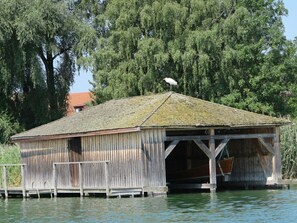 A wooden boathouse with a roof and a dock extending into the water.