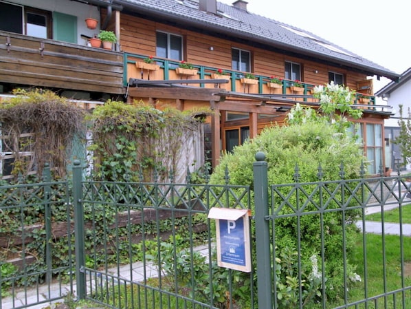 A wooden building with a balcony, a green fence, and a parking sign.