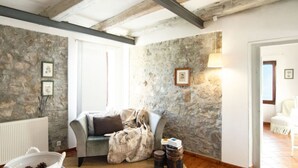 A cozy room with a stone wall, a wooden floor, a white radiator, a grey sofa, and a white chair. - Villa Garibaldino (Podenzana)