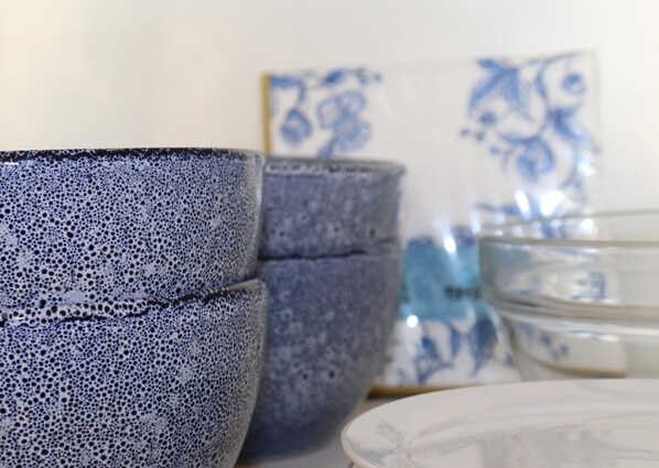 Ceramic cups and bowls with a speckled pattern, a clear glass bowl, and a white plate with a floral design. - Sunny Apartment Directly on the Heegermeer (Heeg)