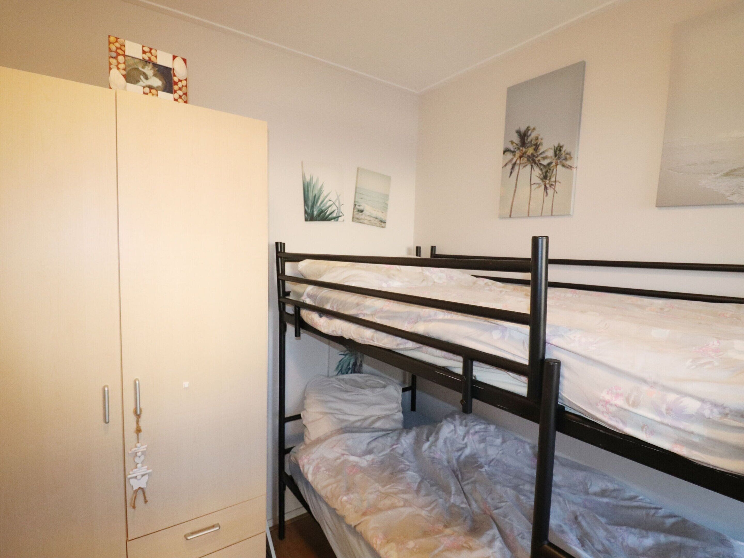 A bunk bed room with a wardrobe, a plant, and a picture of palm trees on the wall.