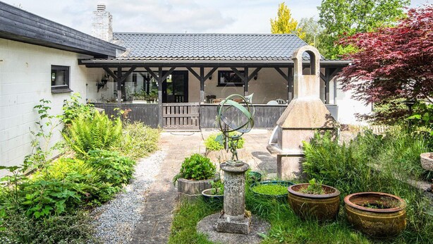 A rustic garden with a stone fountain, potted plants, and a wooden pergola. - 8 Person Holiday Home in Ebeltoft (Ebeltoft)