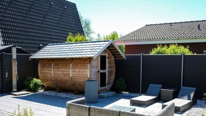A modern outdoor patio with a wooden barrel structure, wicker furniture, and a gravel ground. - Maiwaldo House Comfortable Vacation Home (Wurster Nordseeküste)