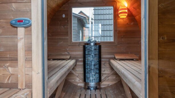 A sauna with wooden benches and a central column, featuring a window and a wall-mounted thermometer. - Maiwaldo House Comfortable Vacation Home (Wurster Nordseeküste)
