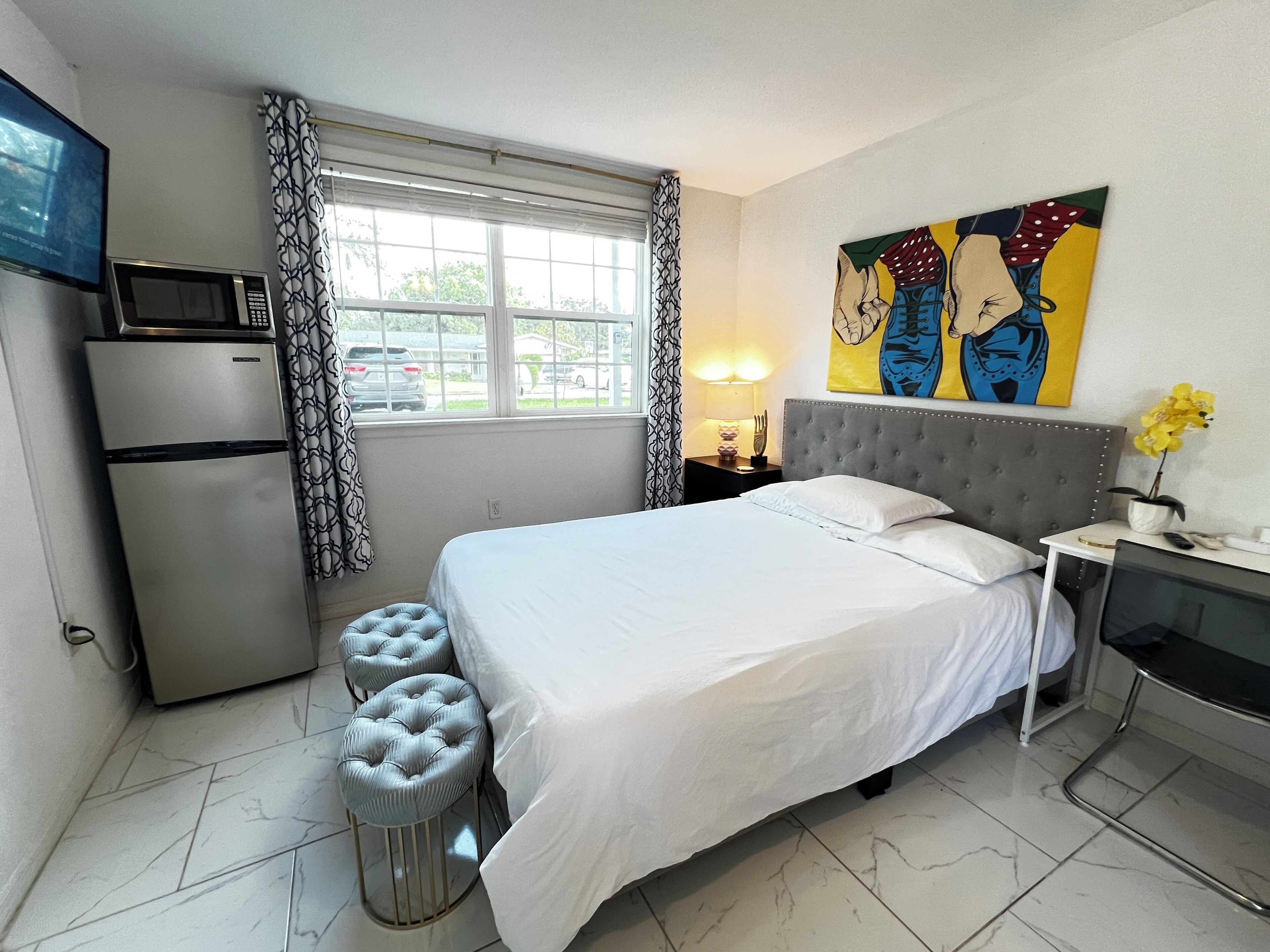 Ein Hotelzimmer mit Bett, Fernseher, Mikrowelle, einem kleinen Tisch mit Lampe und einem Bild an der Wand.