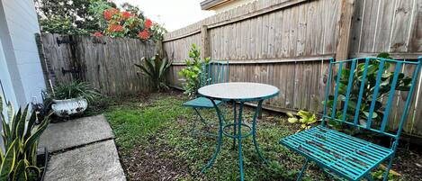 A backyard with a wooden fence, a round table, and a blue metal bench.