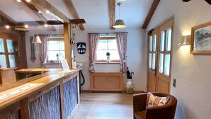 Un espace d’accueil comprenant un comptoir en bois, un bureau de réception, un coin salon avec un canapé et un fauteuil, ainsi qu’une fenêtre avec des rideaux.