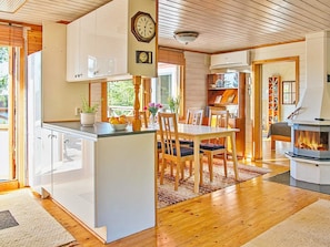 A modern kitchen with a central island, dining area with chairs, a fireplace, and a clock on the wall.