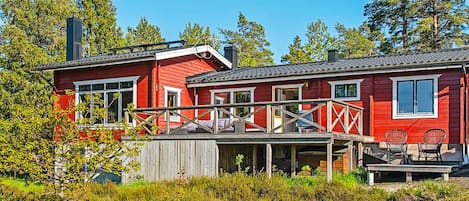 A red cabin with a deck and outdoor seating, surrounded by dense greenery and trees.