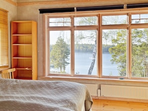 A room with a large window overlooking a lake, a wooden bookshelf, and a bed with a quilted blanket.