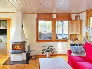 A cozy living room with a wood-burning stove, a red sofa, and a view through large windows.