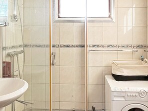 Bathroom features a clear shower enclosure, washing machine, and a white sink.