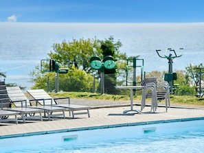 Una piscina con equipo de ejercicio, sillas de descanso y vista al mar.
