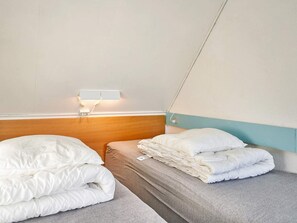 Une chambre d’hôtel avec deux lits simples, une tête de lit en bois, une lampe fixée au mur et un design simple et épuré.