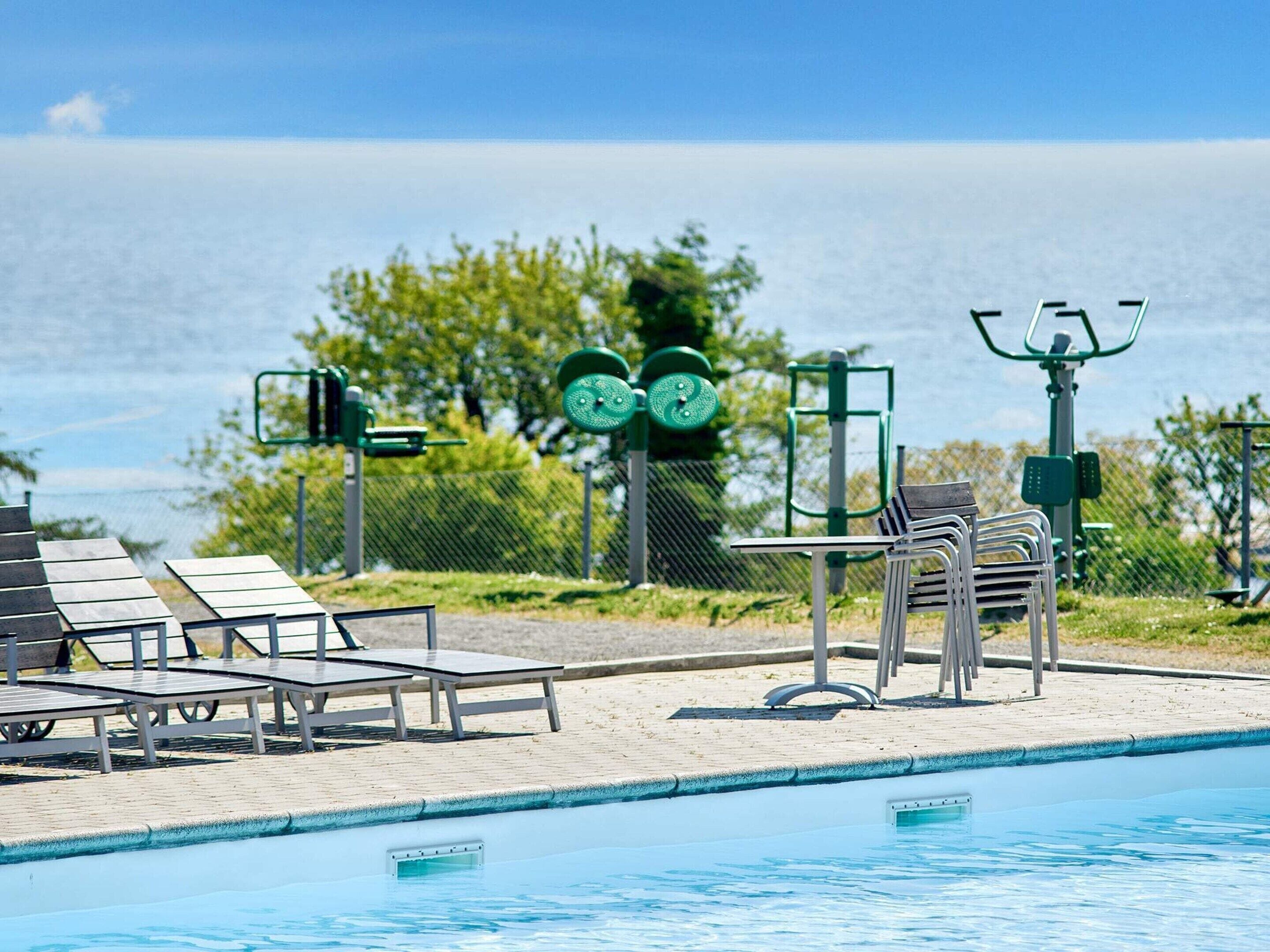 A swimming pool with exercise equipment, lounge chairs, and a view of the sea.