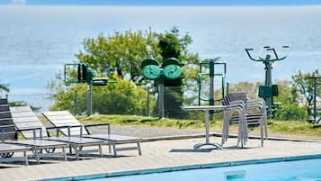Una piscina con equipo de ejercicio, sillas de descanso y vista al mar.