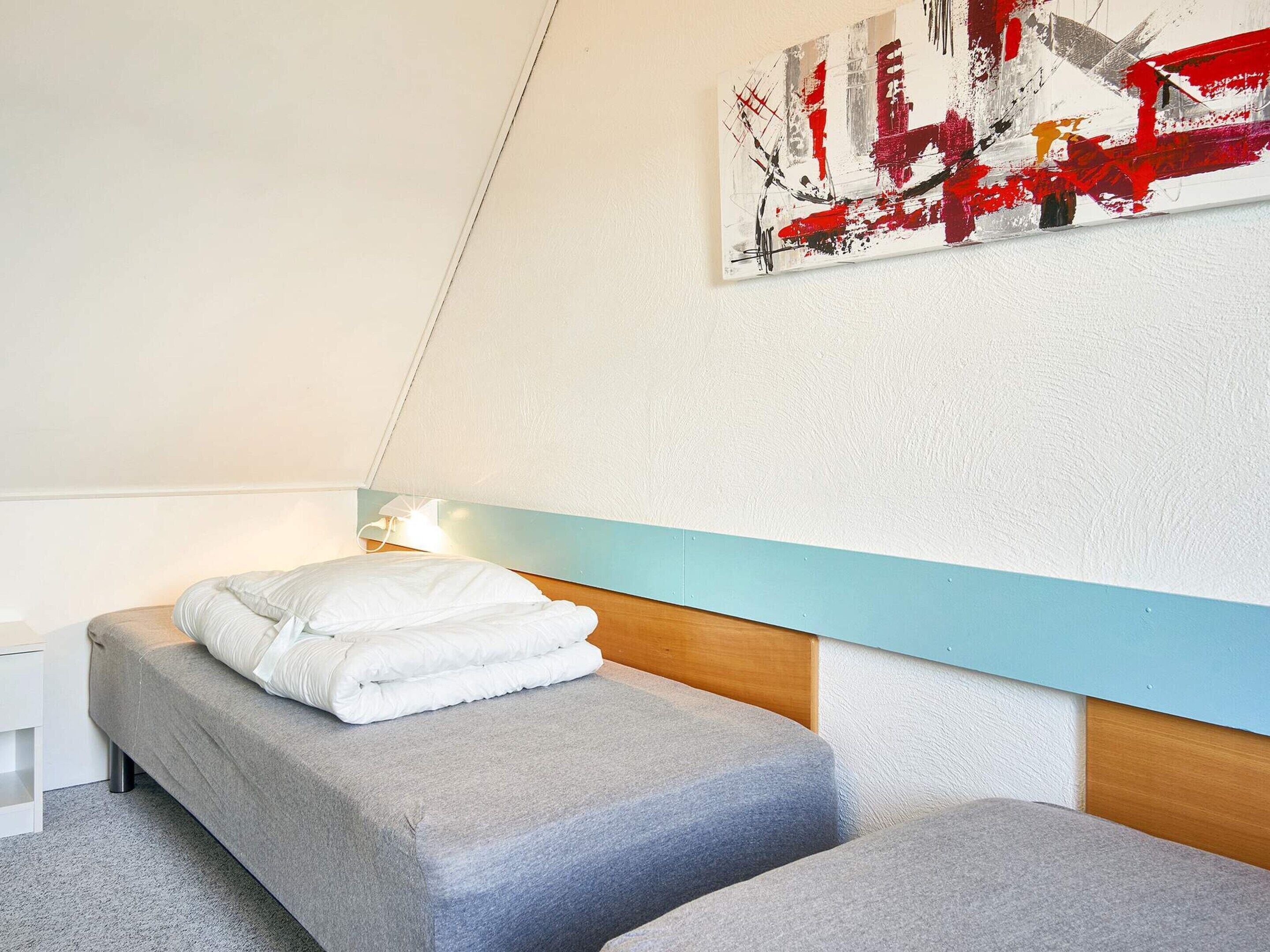 A bedroom with a bed, a bedside table, a wall-mounted artwork, and a light fixture.