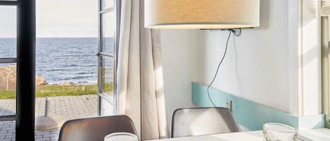 A room with a table, two chairs, a lamp, and a view of the sea.