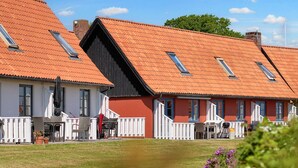 A row of traditional red-roofed cottages with white railings, a grassy lawn, and a clear sky. - 5 Person Holiday Park Home in Gudhjem (Gudhjem)