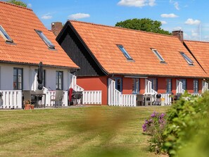 Une rangée de charmantes maisons traditionnelles aux toits rouges et aux balustrades blanches, avec une pelouse verdoyante et un ciel dégagé.