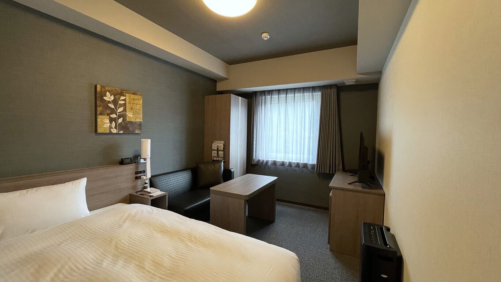 A hotel room with a bed, a desk, a chair, a TV, and a window with curtains.