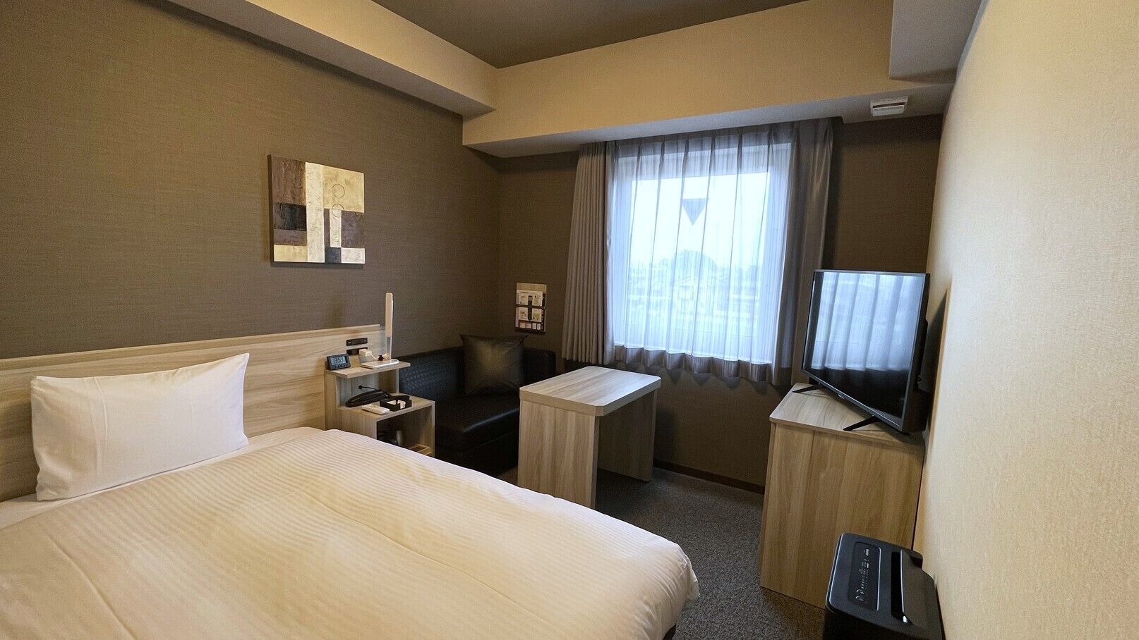 A hotel room with a large bed, a desk, a television, and a window with curtains.