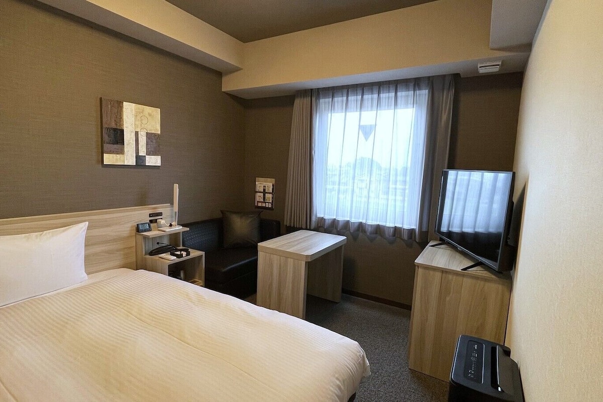 A hotel room with a large bed, a desk, a television, and a window with curtains.