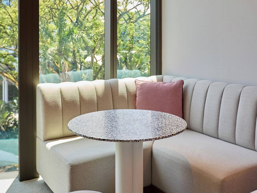 Un salón moderno con un sofá seccional color beige, una mesa redonda y vistas a espacios verdes y edificios.