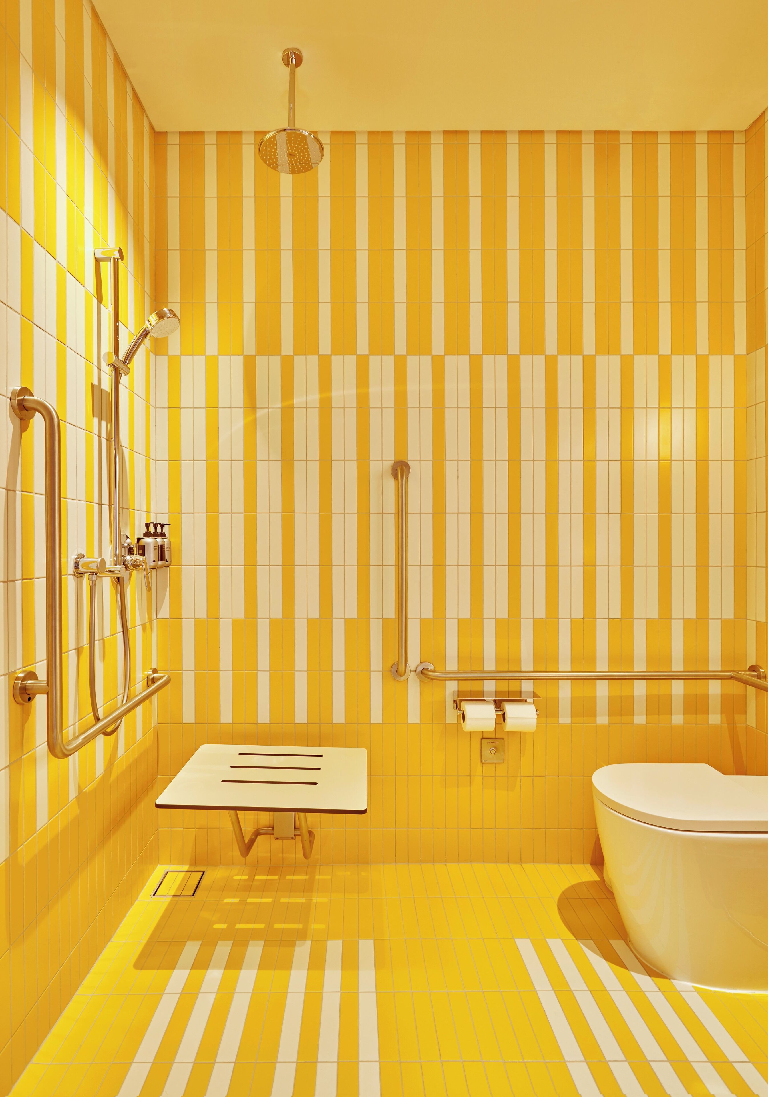Une salle de bain avec des carreaux rayés jaunes et blancs, un lavabo blanc et des toilettes blanches.