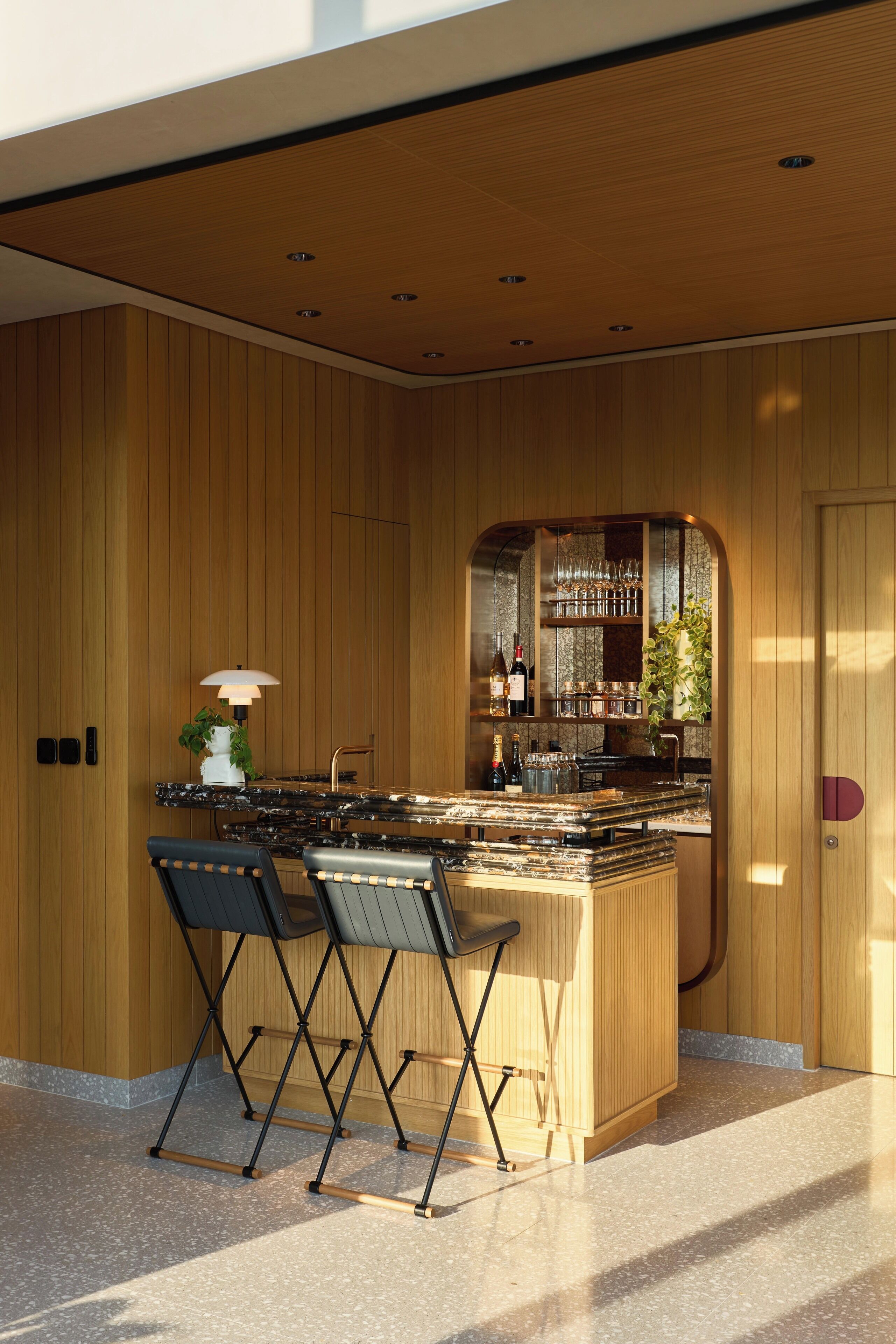 A modern kitchen with wooden paneling, a bar area with wine bottles, and two foldable chairs.