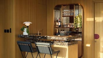 Een moderne keuken met houten lambrisering, een bar met wijnflessen en twee opklapbare stoelen.