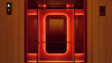 An elevator with a red-lit interior, a circular light fixture above, and a directional sign on the wall.