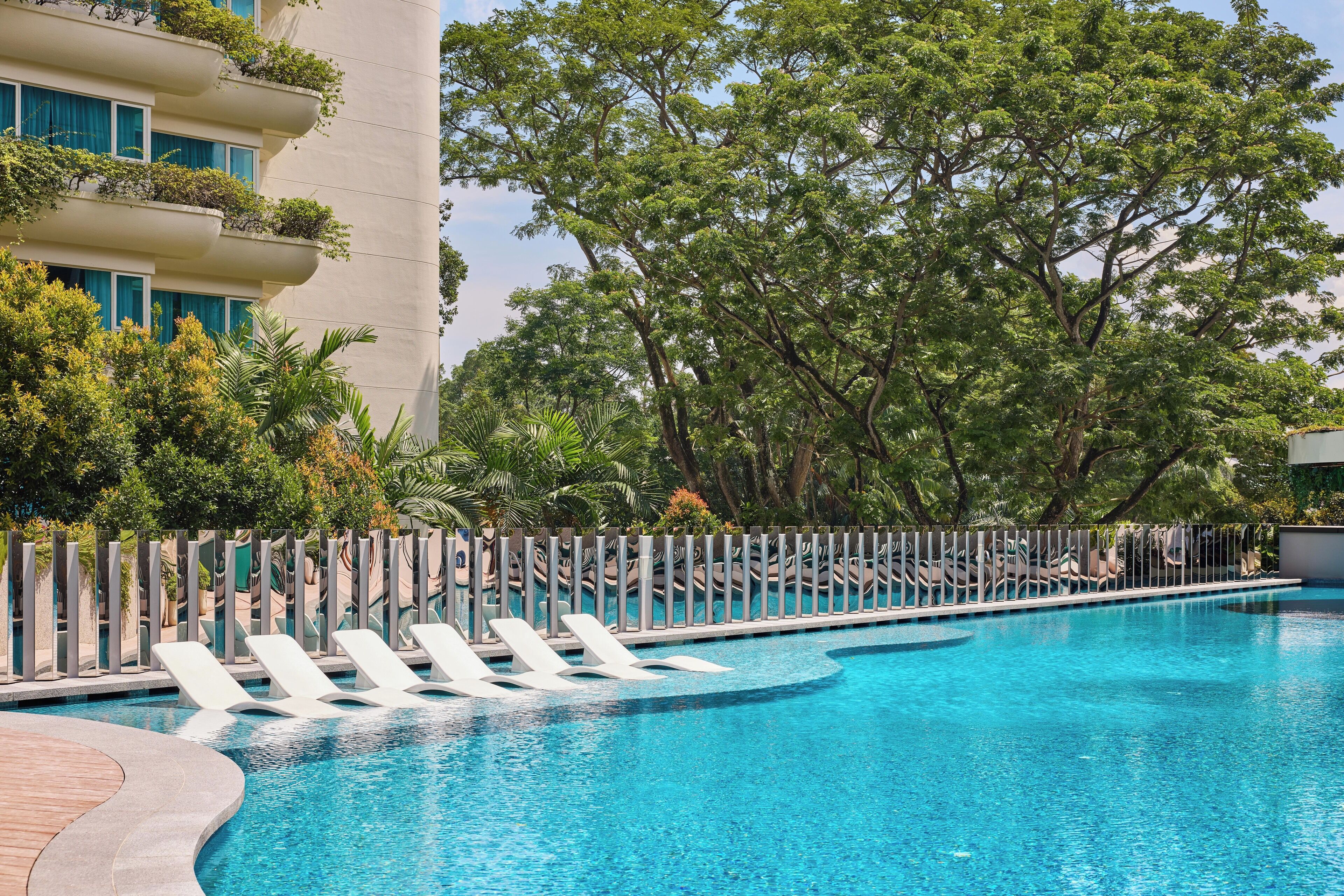 A swimming pool with lounge chairs, surrounded by trees and a building with balconies.