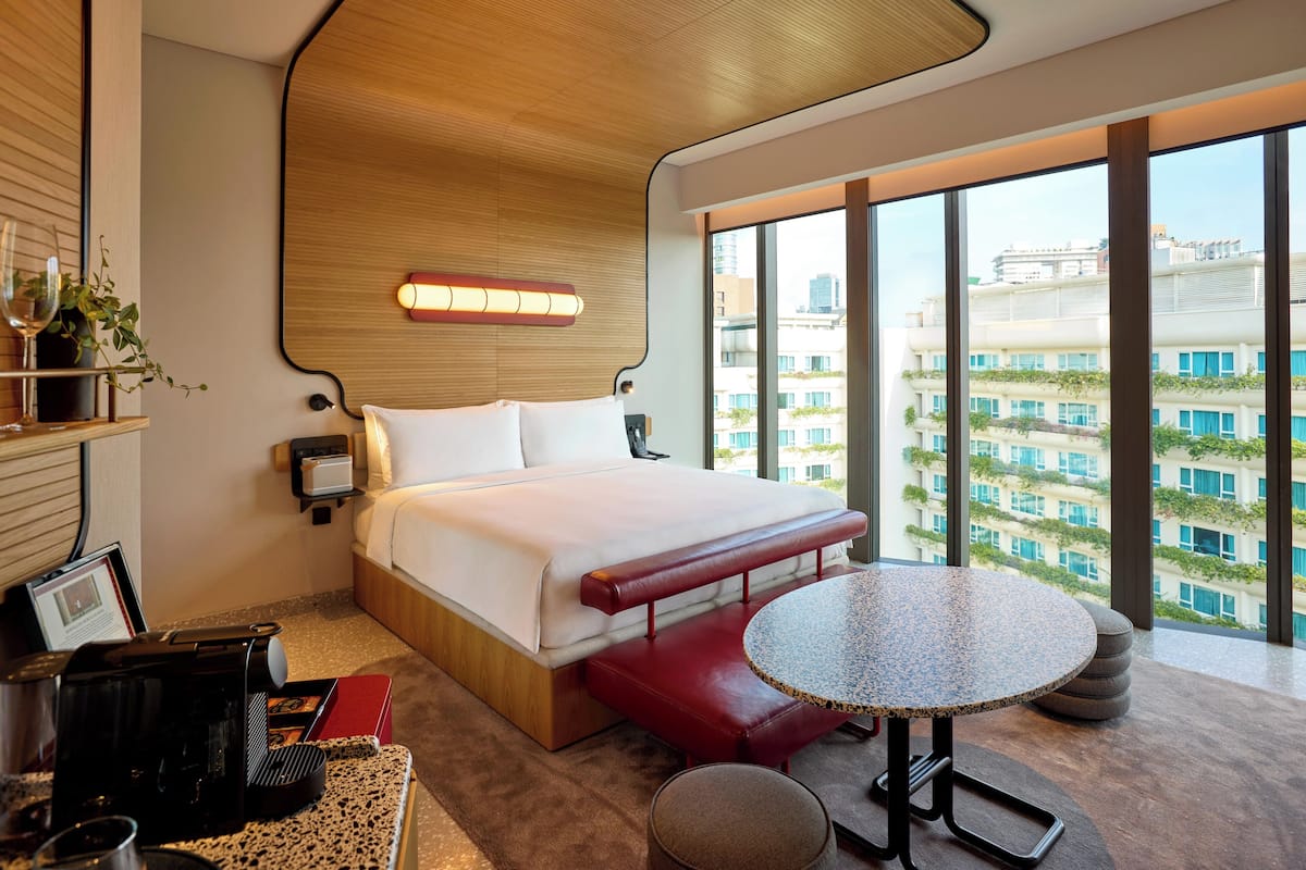 Une chambre d’hôtel moderne, dotée d’un grand lit, d’une table ronde et offrant une vue sur la ville grâce à de grandes fenêtres.