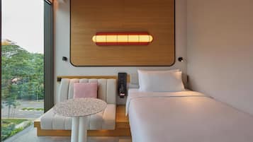 A modern hotel room with a large window, a bed, a sofa, and a small table.
