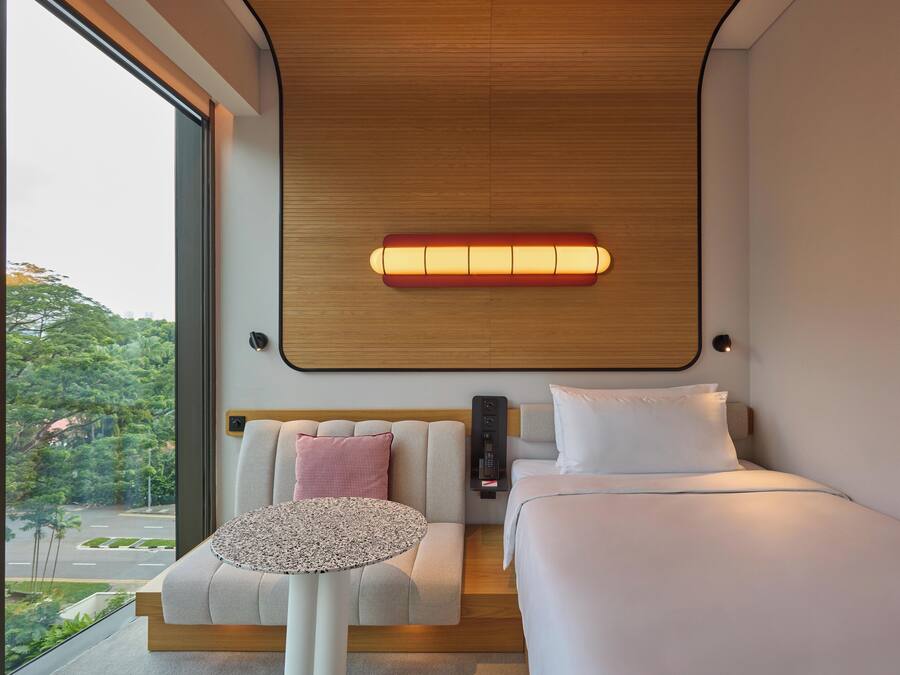 A modern hotel room with a large window, a bed, a sofa, and a small table.