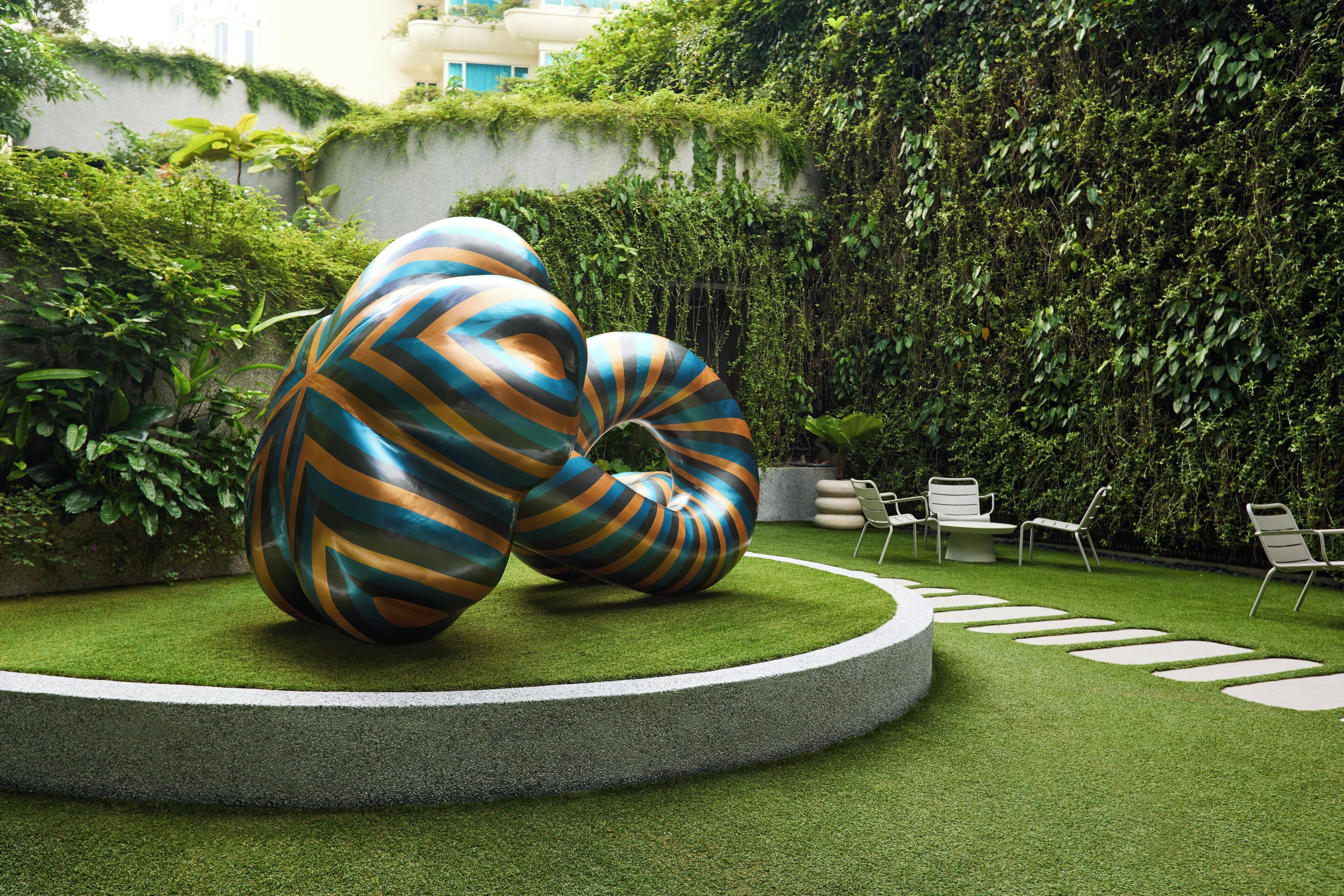 A circular garden with artificial grass, two large spiral sculptures, and a seating area with white chairs.