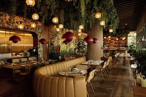 Un restaurant avec des banquettes, des tables et des plantes suspendues.