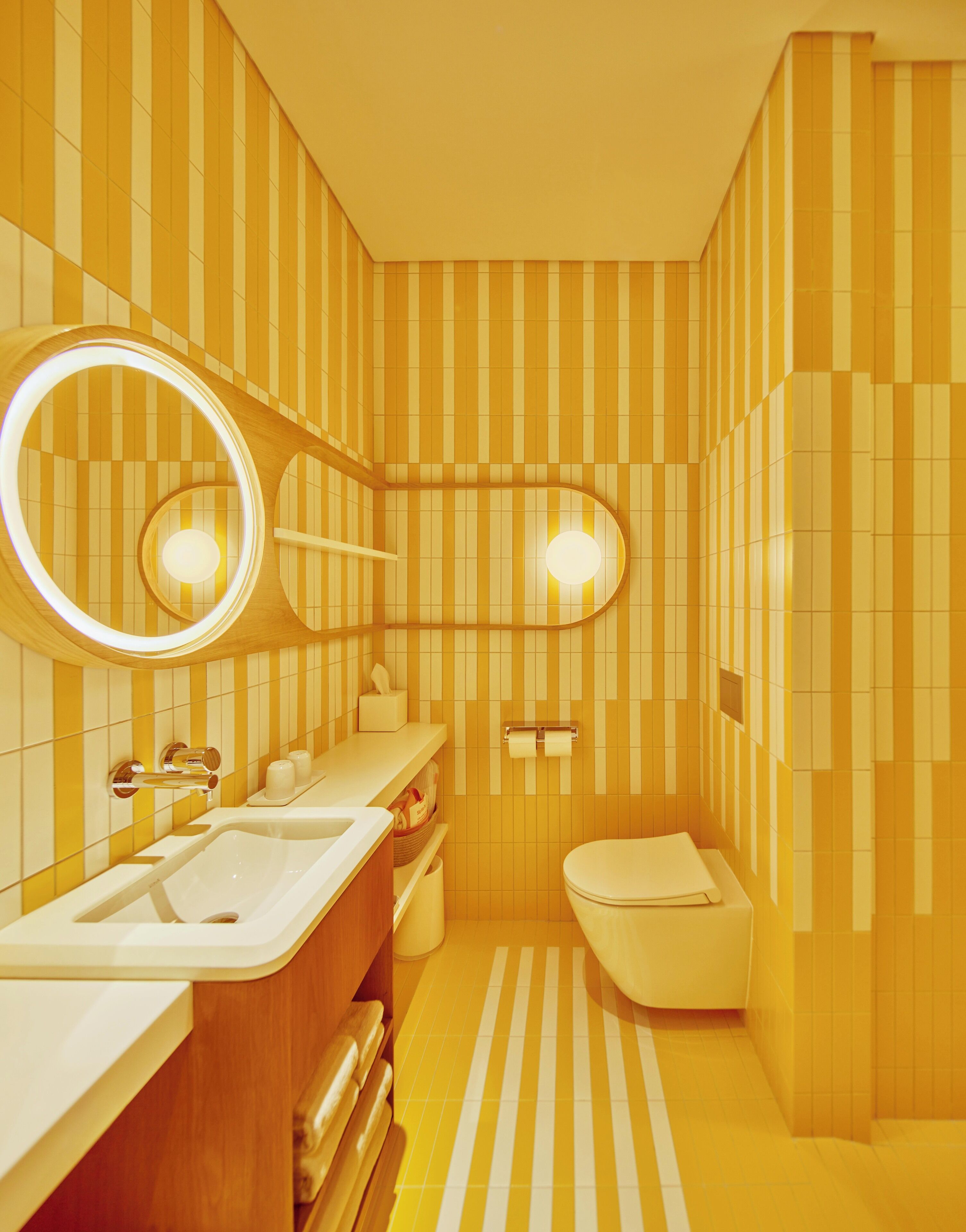 Un baño con paredes a rayas, un lavabo, un inodoro y un espejo con iluminación.