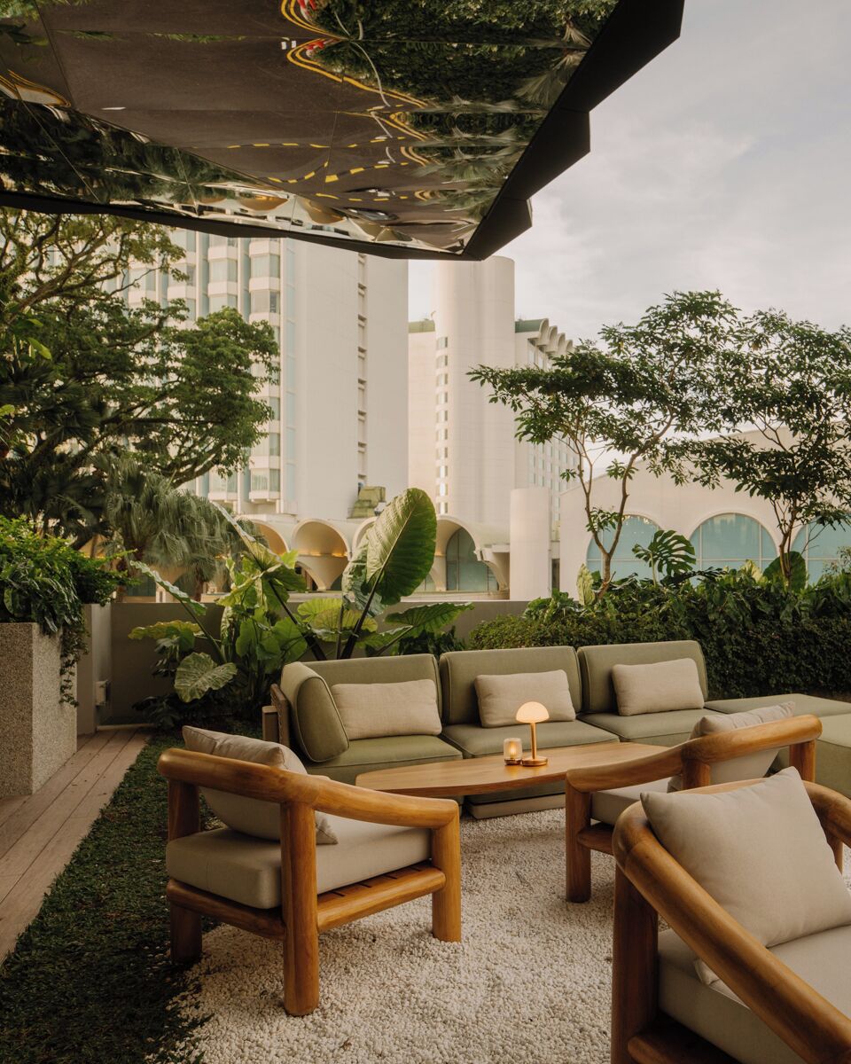 An outdoor seating area with a sofa and chairs, surrounded by greenery and a view of buildings.