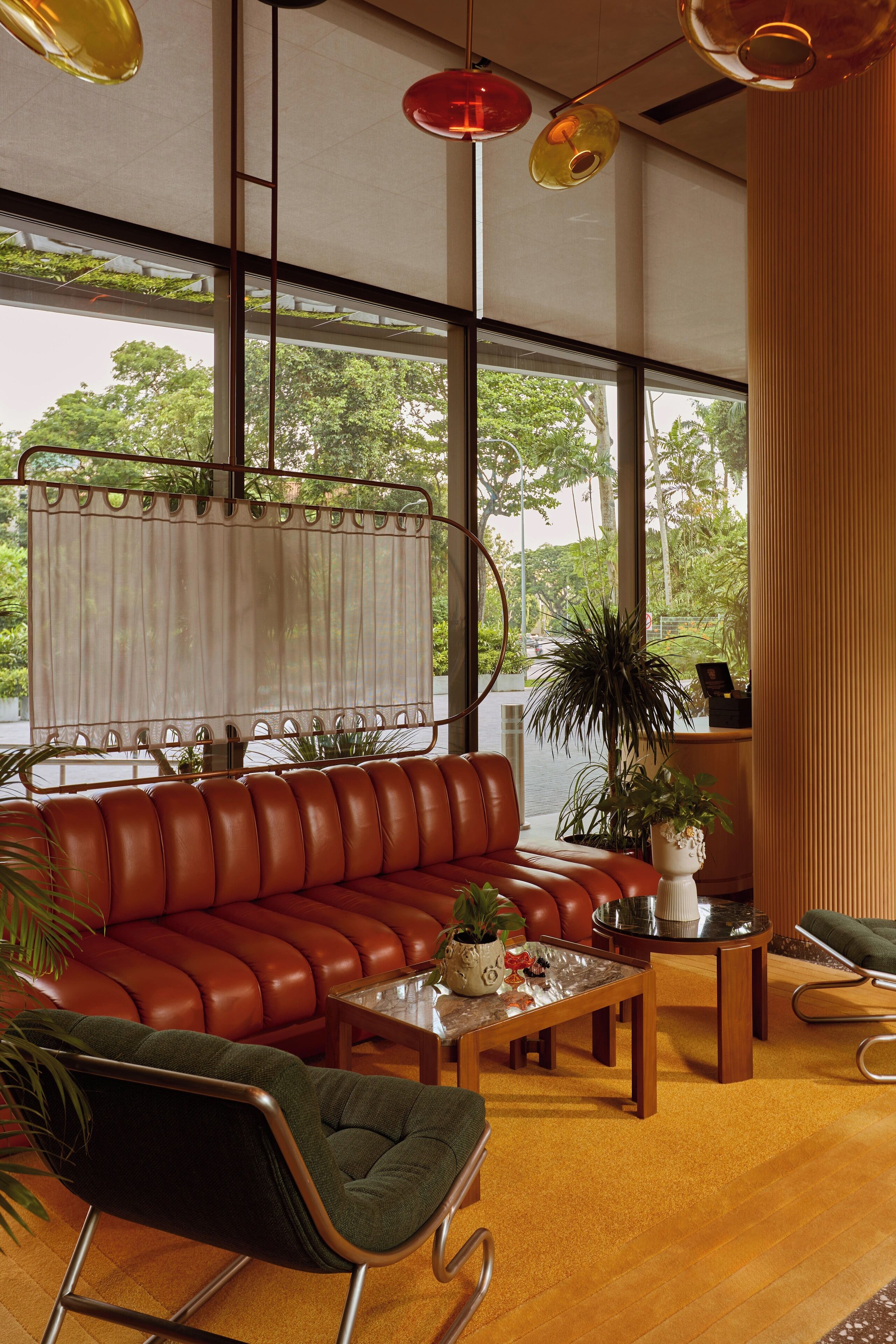 Ein modernes Wohnzimmer mit einem Ledersofa, einem grünen Sessel und einem Couchtisch. Ein großes Fenster bietet Blick auf Bäume und ein Gebäude.