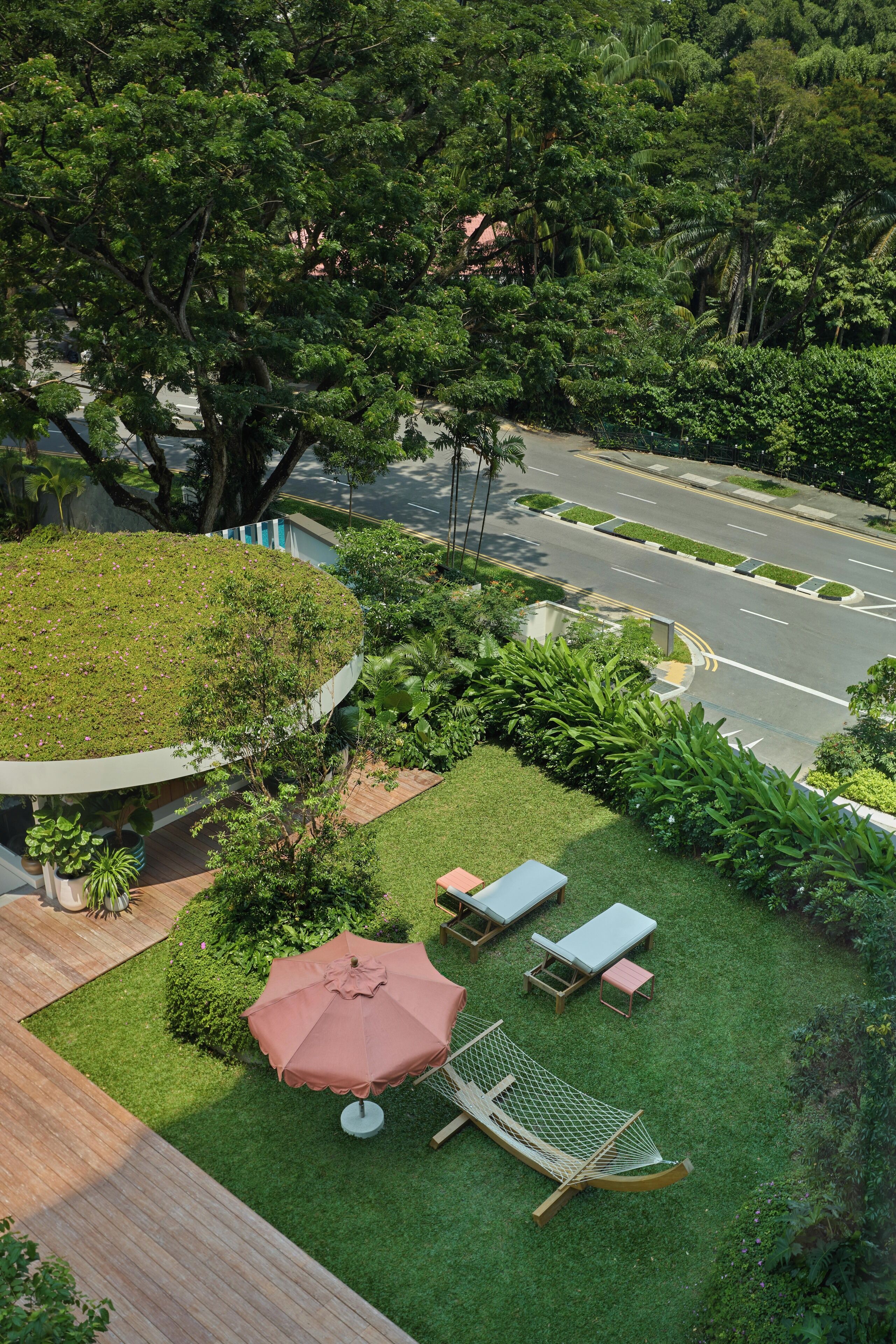A rooftop garden with a circular seating area, a hammock, and a view of a road.