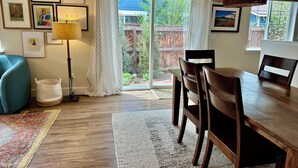 Zona pranzo con tavolo e sedie in legno, una lampada da terra e vista su un patio esterno in legno attraverso una porta di vetro.